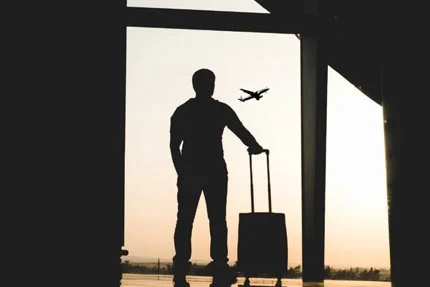 man standing with suitcase looking at airplane